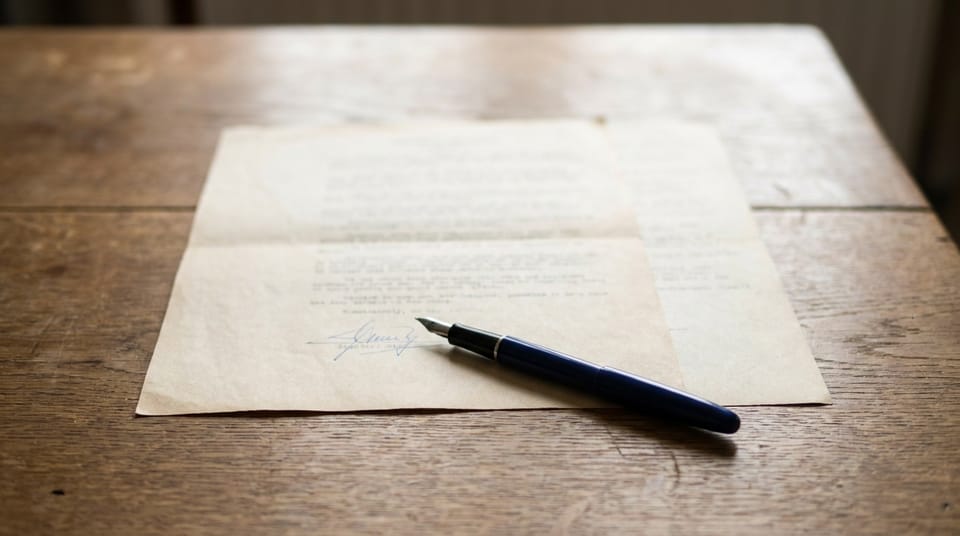 A two-page contract on an oak desk, signed at the foot in ink, a navy fountain pen lying across it.
