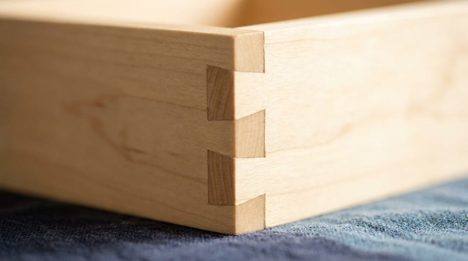 Close view of a tight dovetail joint in pale wood, two pieces fitted perfectly together.