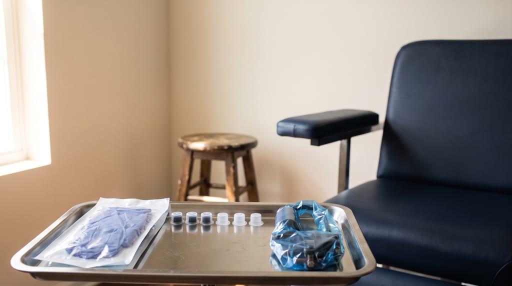 A clean tattoo station: a wrapped machine, sealed ink caps and fresh gloves on a steel tray, a padded chair beyond, blank walls.
