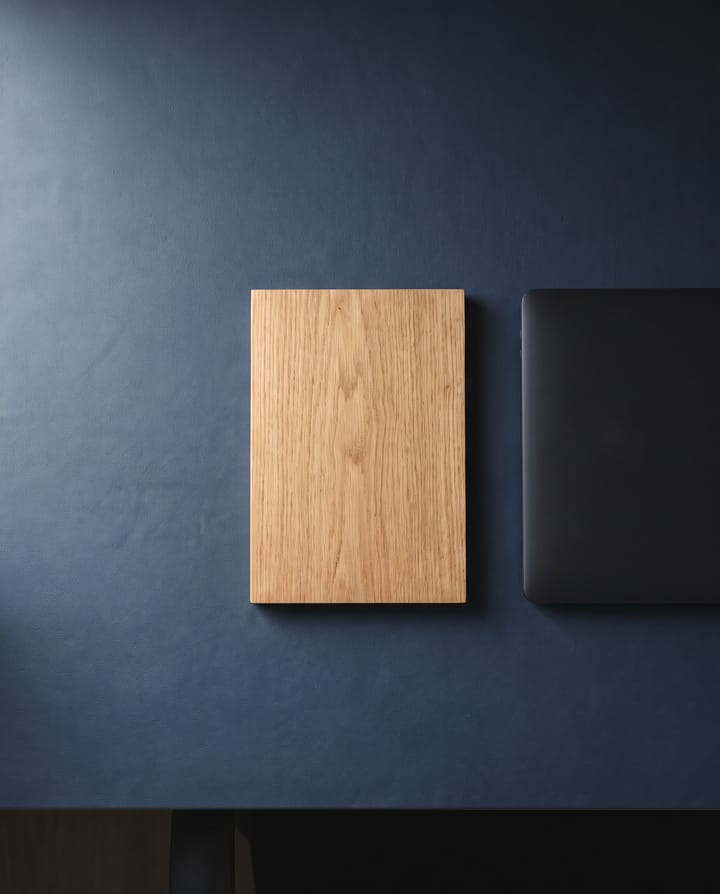 From above: a thin slab of oak beside a closed dark laptop on an otherwise empty navy desk.
