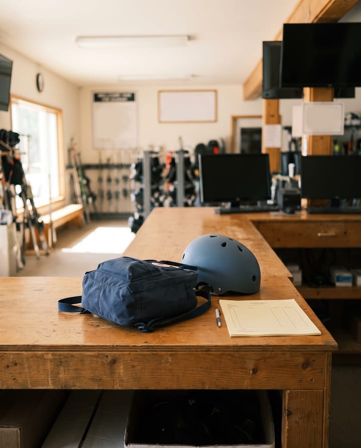 A child's backpack and a small helmet on a rental shop counter beside a paper consent form, the view from behind the counter into the empty shop.