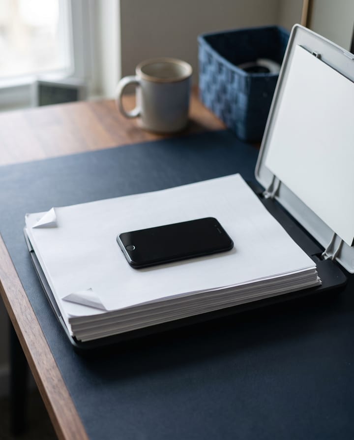 A thick printed agreement on a desk with a dark phone lying on top, a scanner lid open beside it.