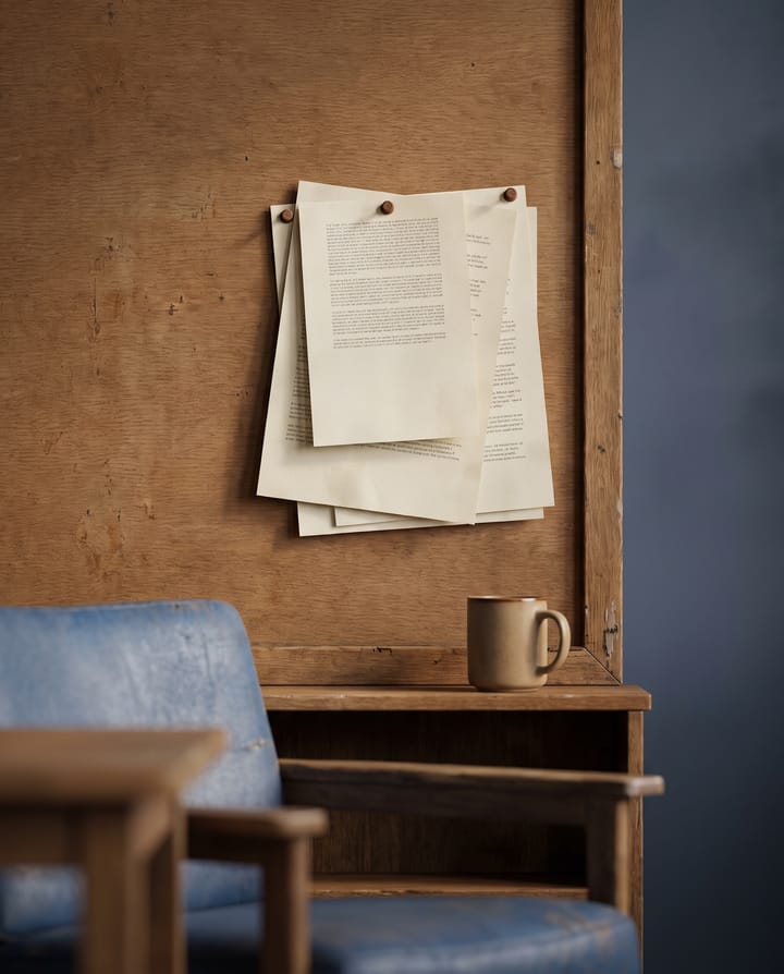 A noticeboard with printed policies pinned over one another, their type too small to read, a coffee cup on the shelf below.